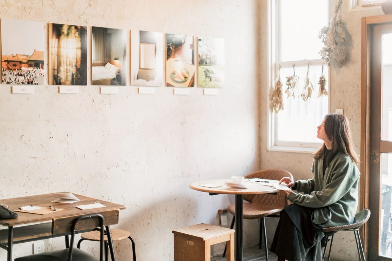 toco.の窓辺でコーヒーを楽しみながら展示作品を見る来場者
